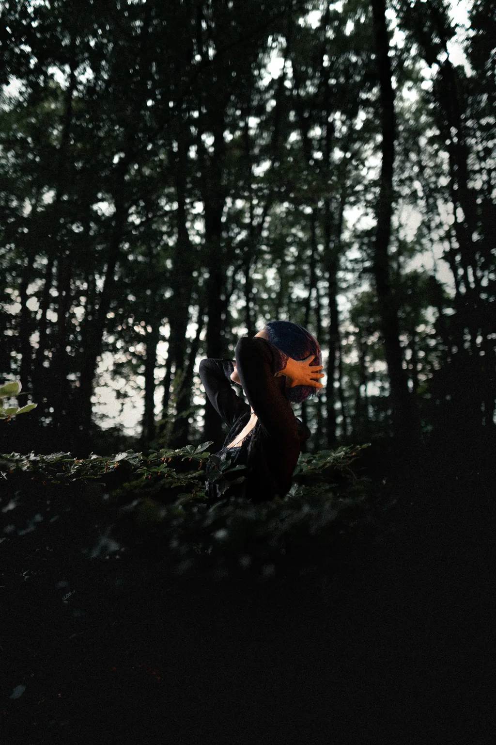 Backlit silhouette of a woman among tall forest trees in a moody Luxembourg outdoor shoot