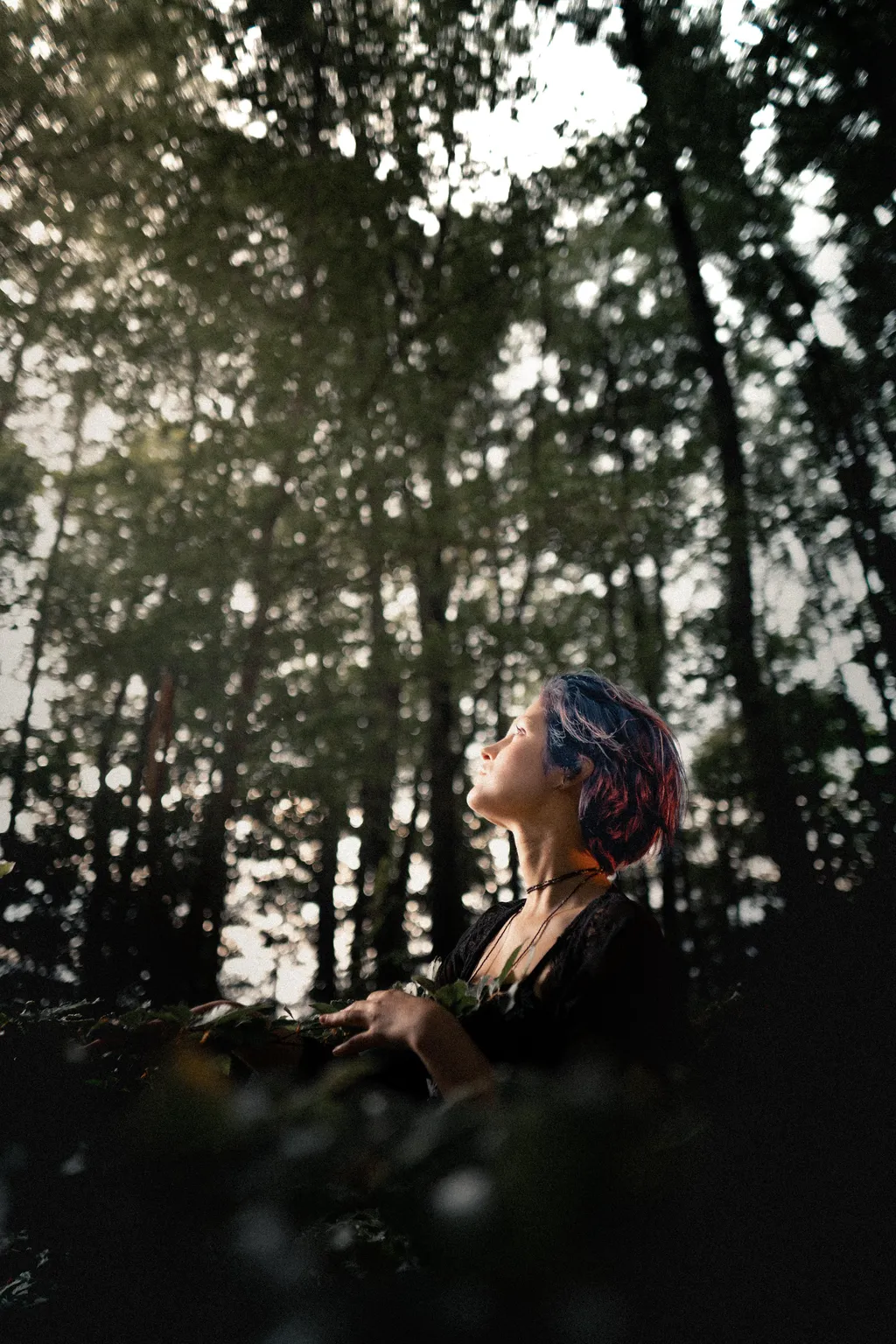 Profile portrait of a woman in soft forest light surrounded by tall trees in Luxembourg