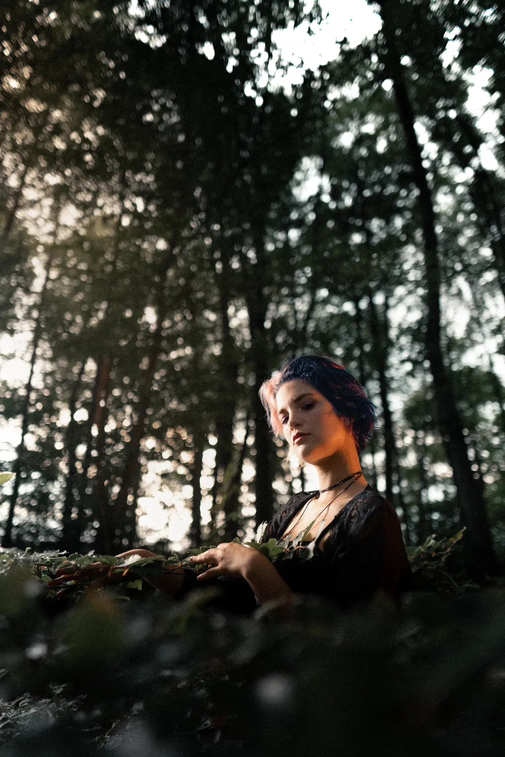 Woman in a black dress seated low among woodland foliage in a Luxembourg forest portrait