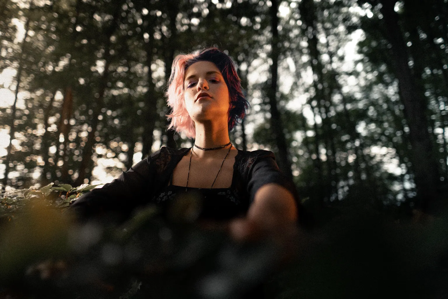 Low-angle outdoor portrait of a woman reaching forward beneath the forest canopy in Luxembourg