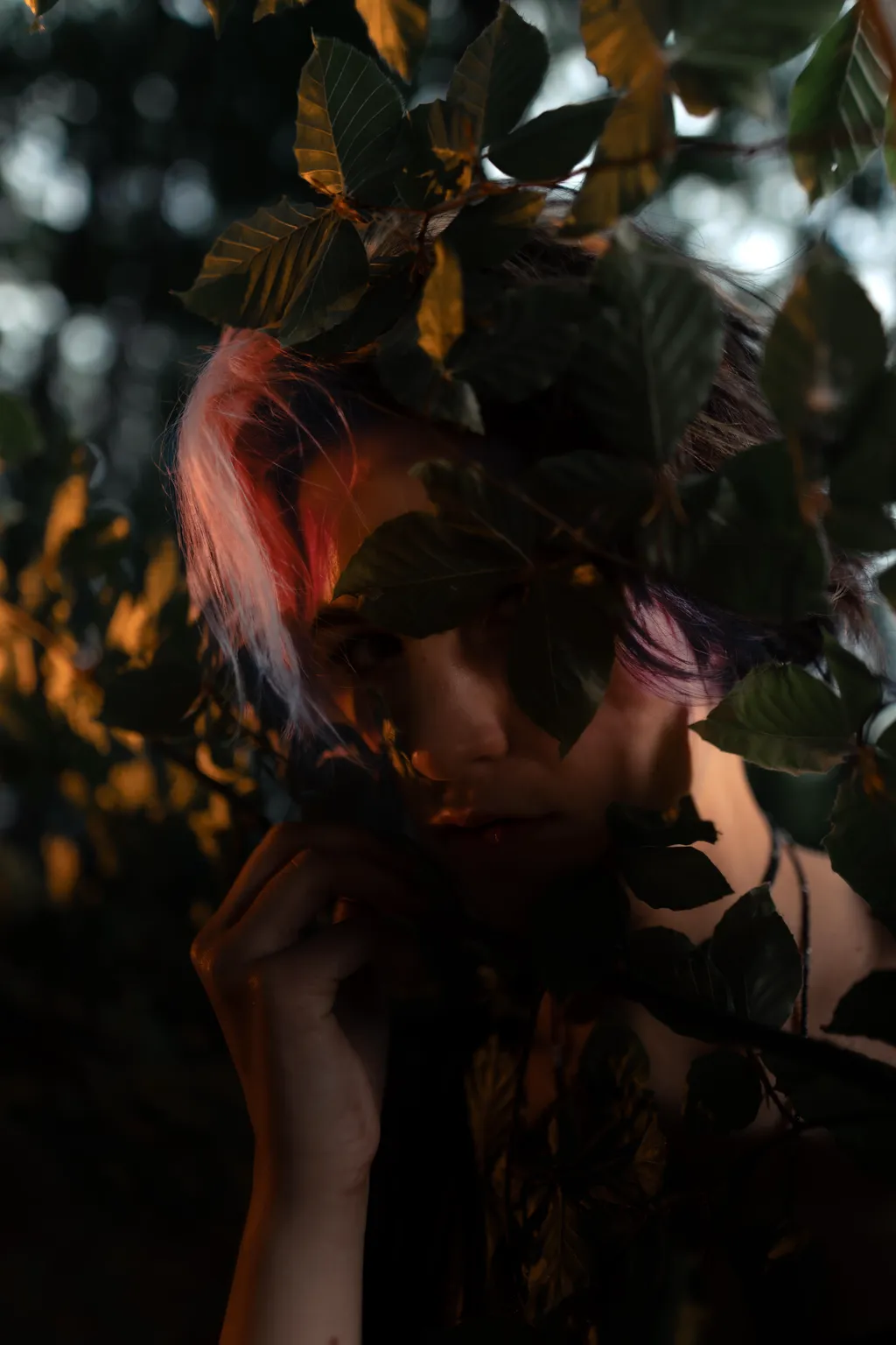 Intimate forest portrait of a woman framed by green leaves with warm rim light, Luxembourg