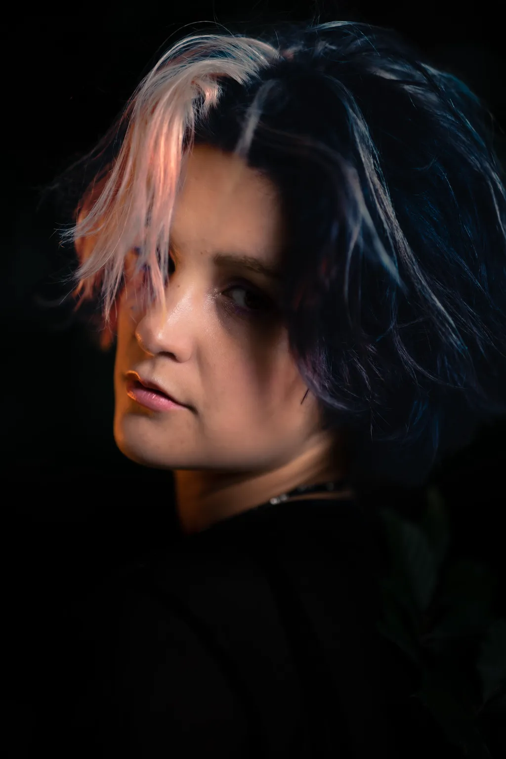 Dramatic studio-style portrait of a woman with pink and dark hair against a black background