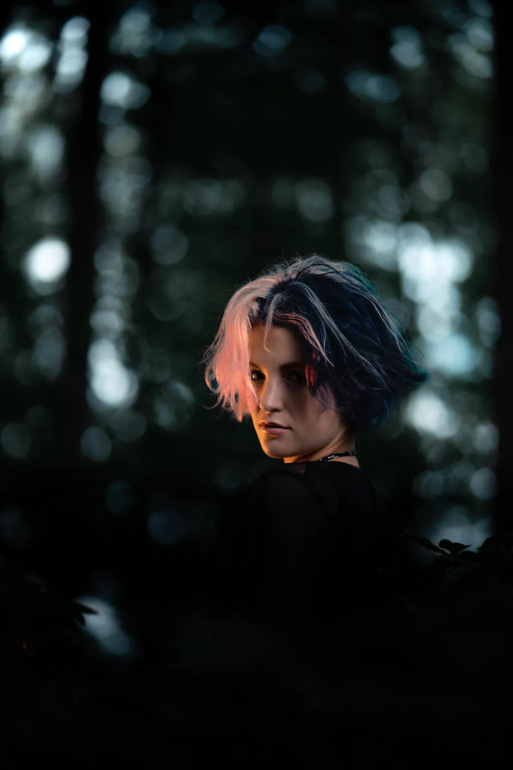 Woman in a black dress glancing over her shoulder amid blurred forest bokeh in Luxembourg