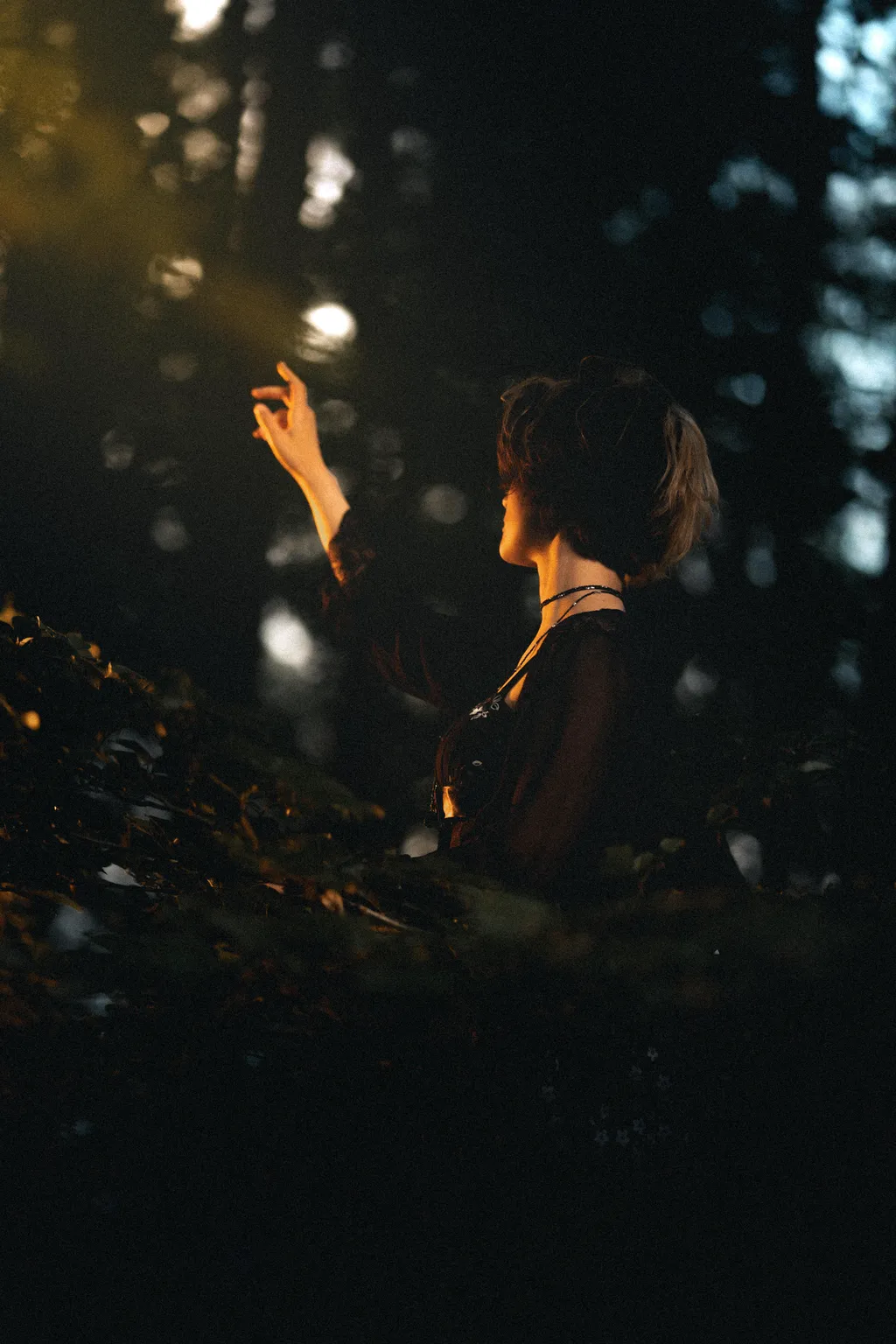 Woman raising her hand toward a shaft of golden forest light in a Luxembourg outdoor portrait