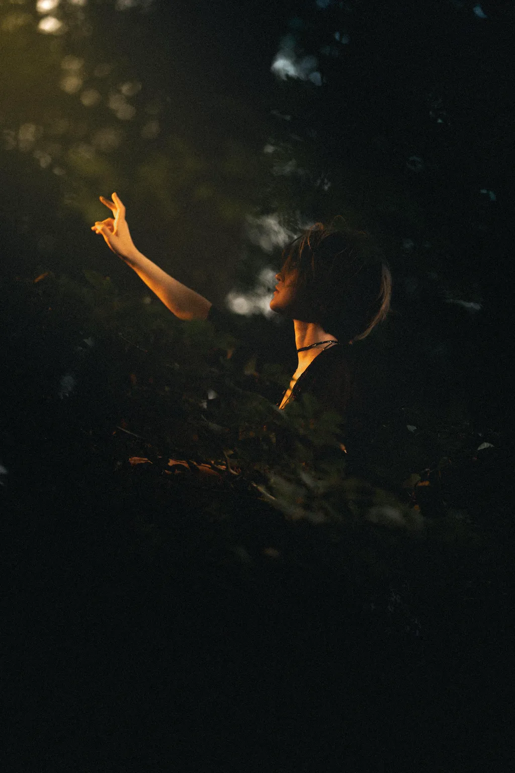 Backlit profile of a woman gesturing in dense dark woodland during a Luxembourg forest shoot