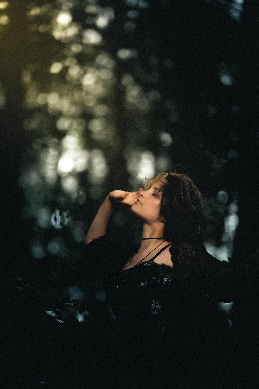 Woman tilting her head back with hand to face in soft forest light, Luxembourg outdoor portrait