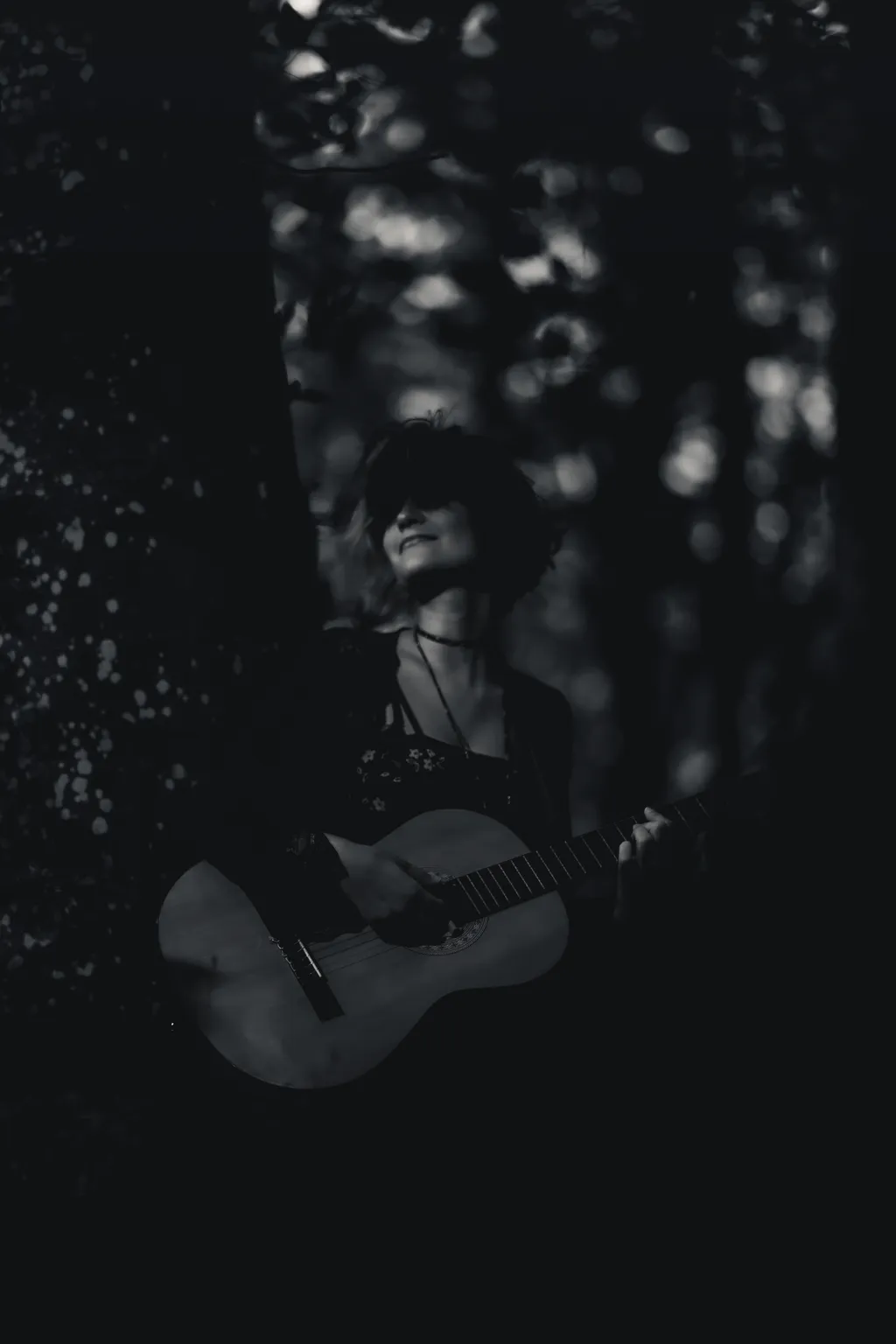 Black-and-white forest portrait of a smiling woman playing acoustic guitar in Luxembourg woods