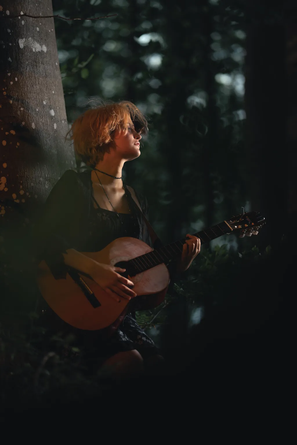 Woman cradling an acoustic guitar in warm low light within a Luxembourg forest setting