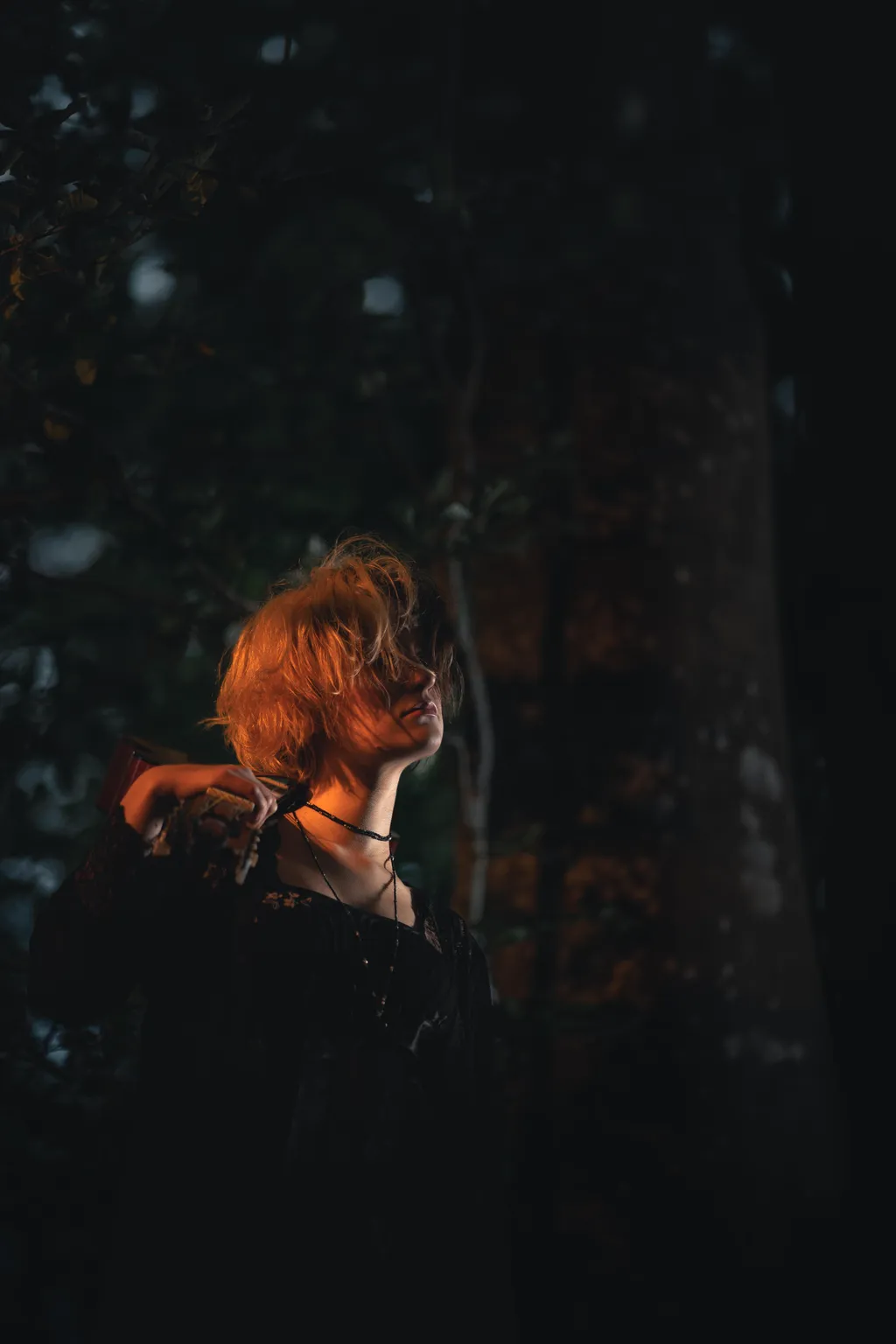 Profile of a woman with red-lit hair touching her neck in dark Luxembourg woodland