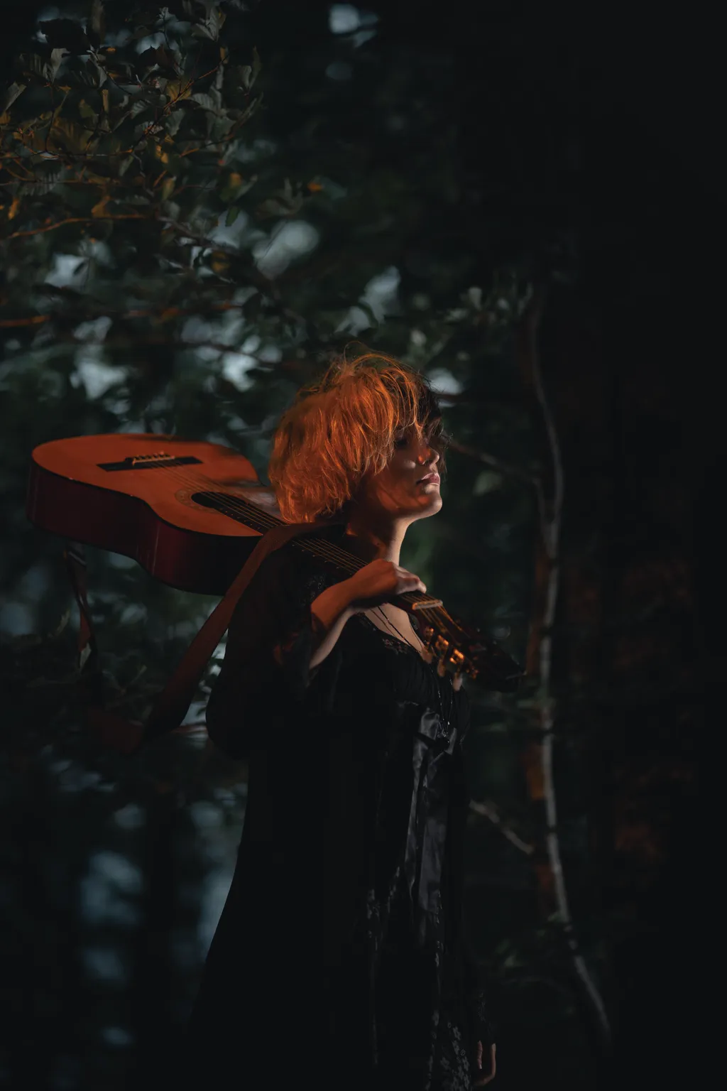 Woman carrying an acoustic guitar over her shoulder in twilight Luxembourg woodland