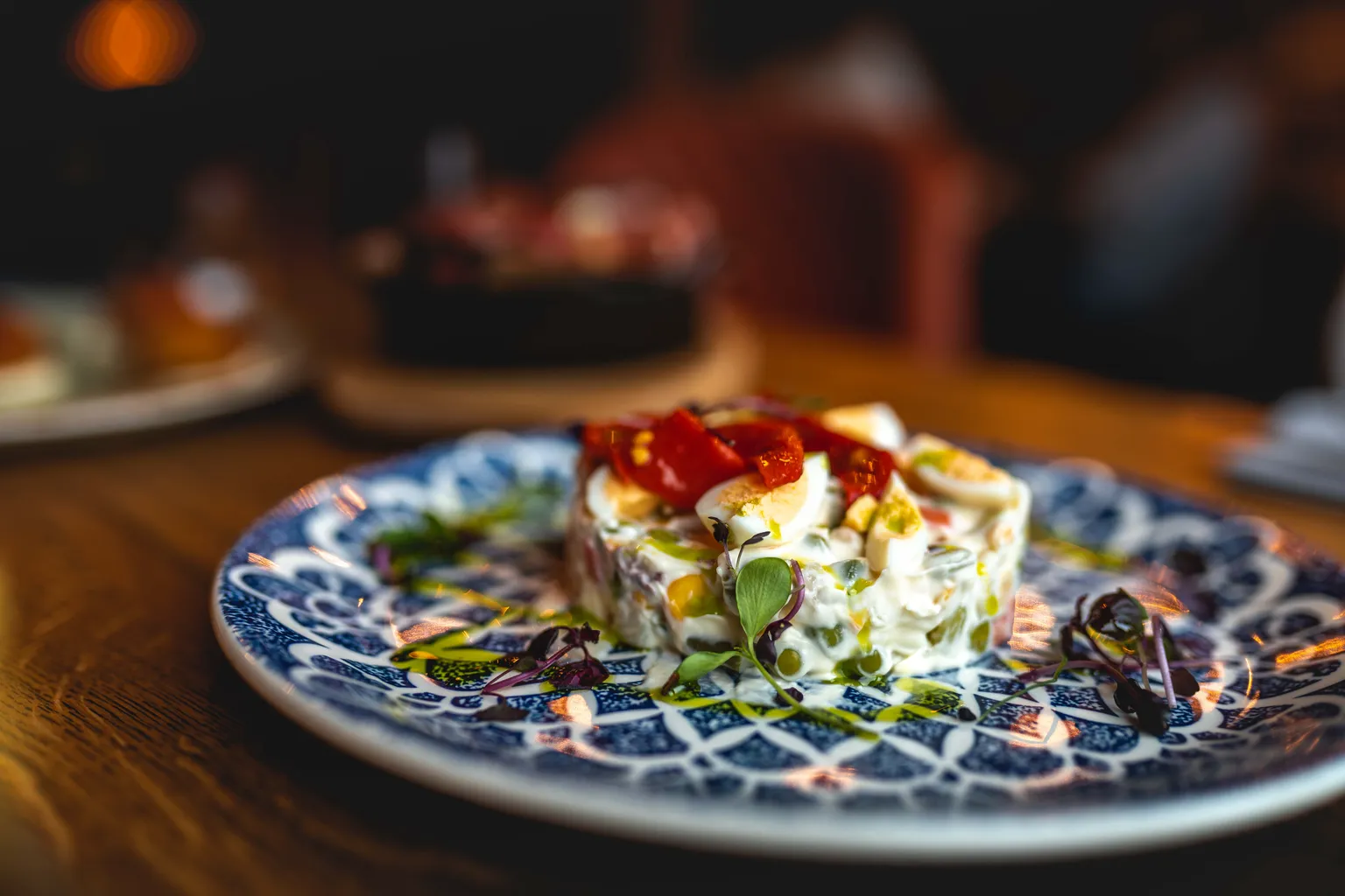 Plated potato salad topped with roasted red pepper and microgreens on an ornate blue-and-white plate, food photography Luxembourg