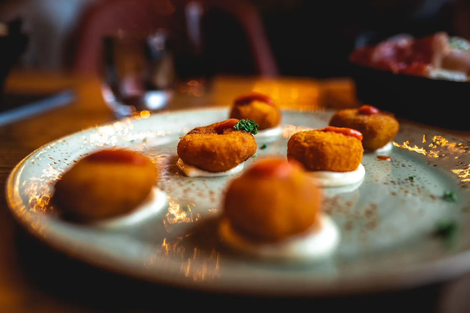 Golden fried croquetas drizzled with red sauce on a stoneware plate, restaurant food photographer Luxembourg