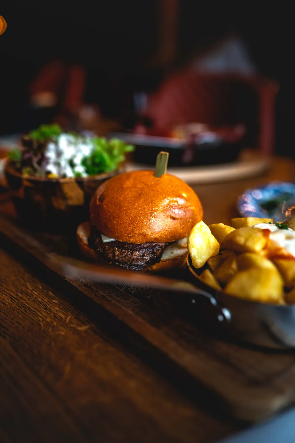 Brioche burger plated with side salad and golden potatoes on a board, moody Luxembourg restaurant lighting