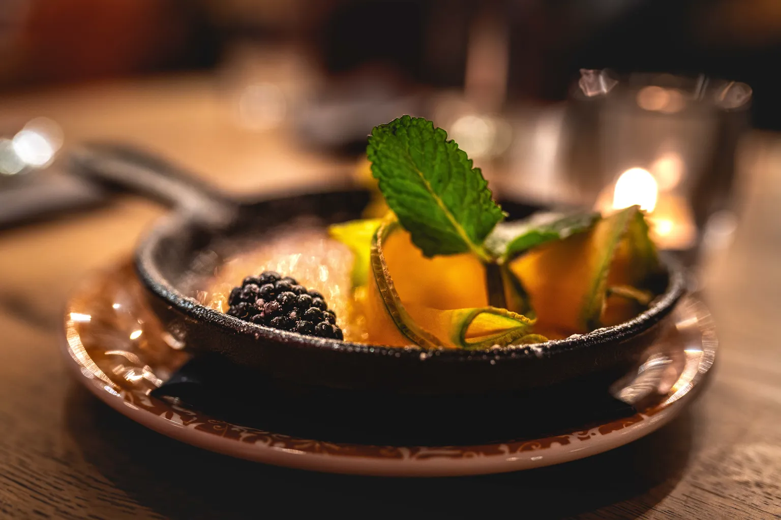 Crème brûlée in a cast-iron skillet garnished with mint, blackberry and mango by candlelight