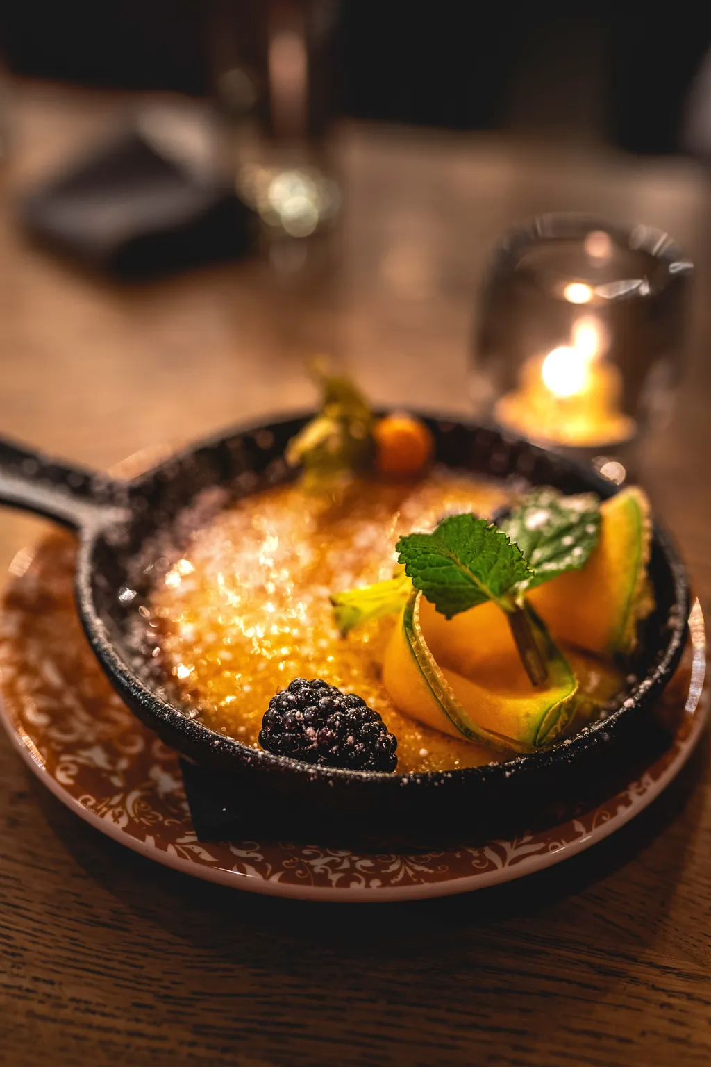 Skillet dessert with caramelised top, mint and physalis beside a flickering candle, intimate restaurant setting
