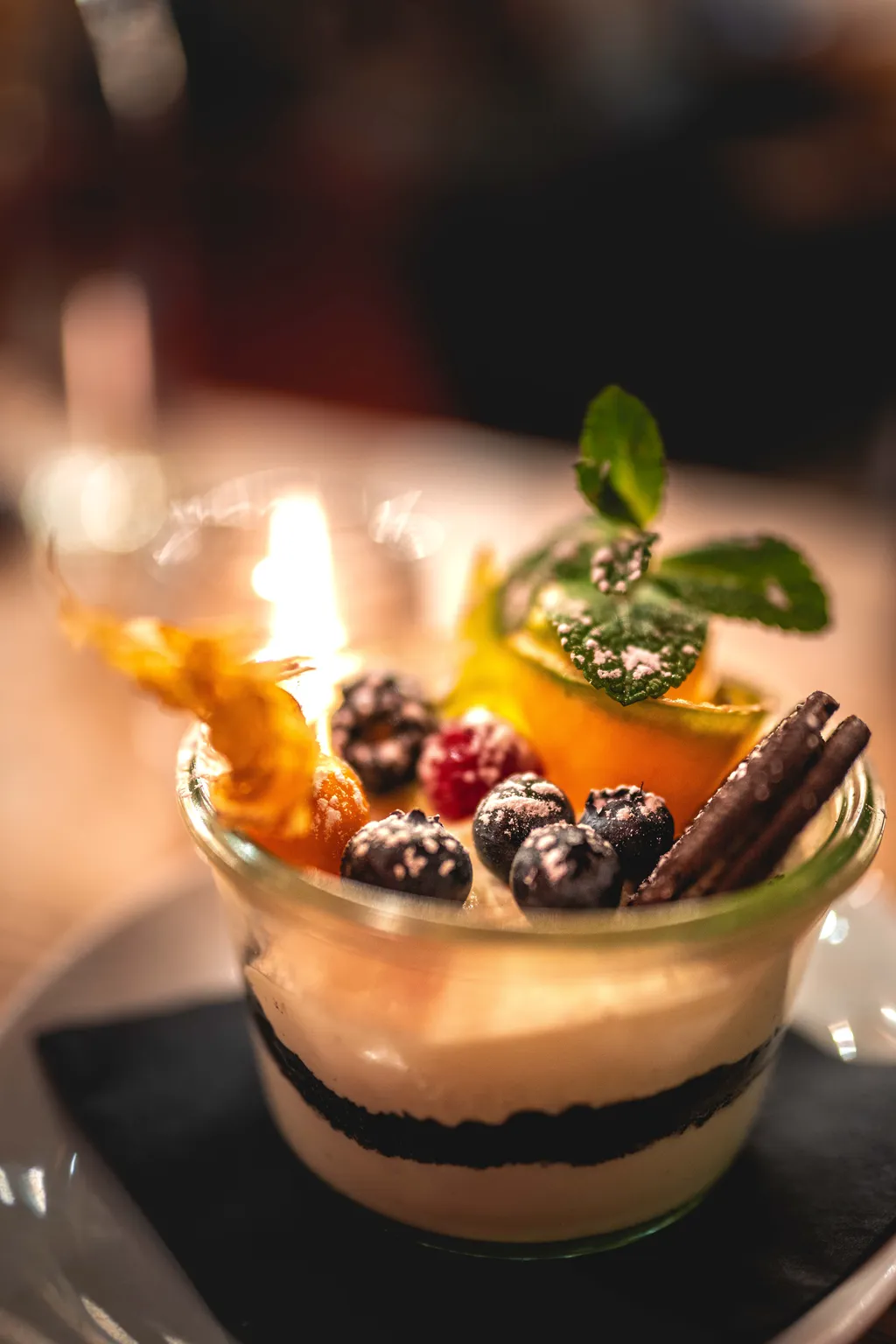 Layered mousse trifle in a glass jar topped with blueberries, raspberry, mint and a cinnamon stick