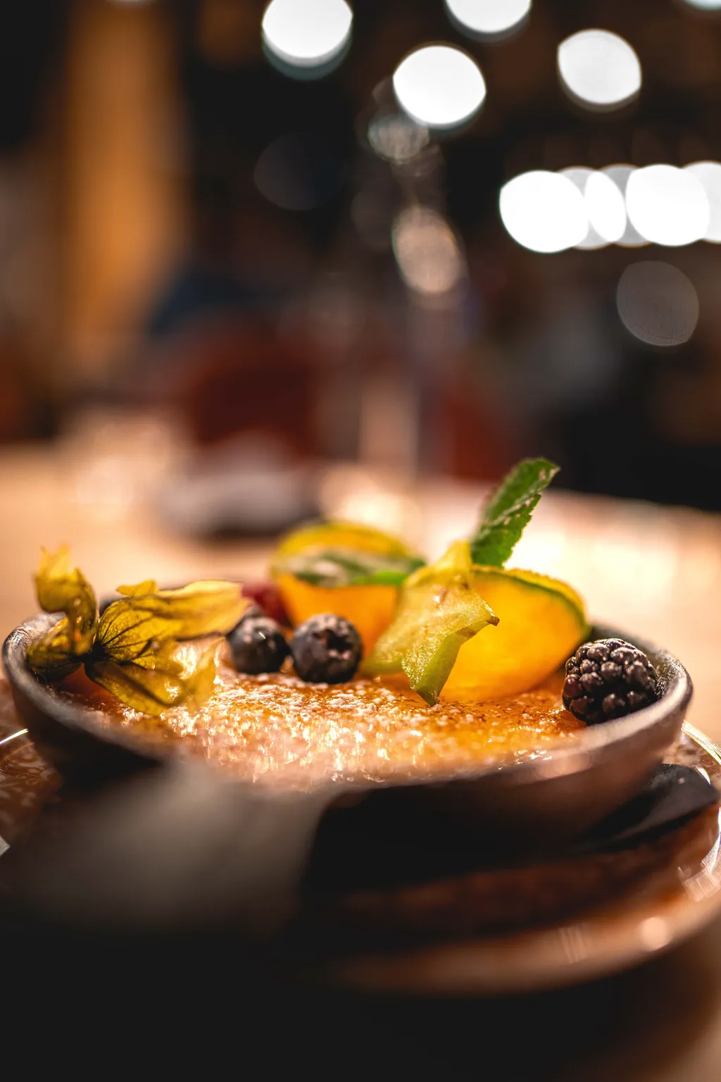 Crème brûlée on a wooden board with mango, kiwi and berries, premium restaurant food photography Luxembourg