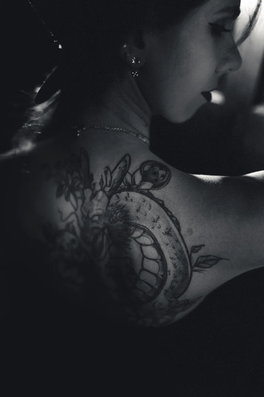 Intimate noir portrait detail: a woman's tattooed shoulder and back in profile, finely lit in black and white.