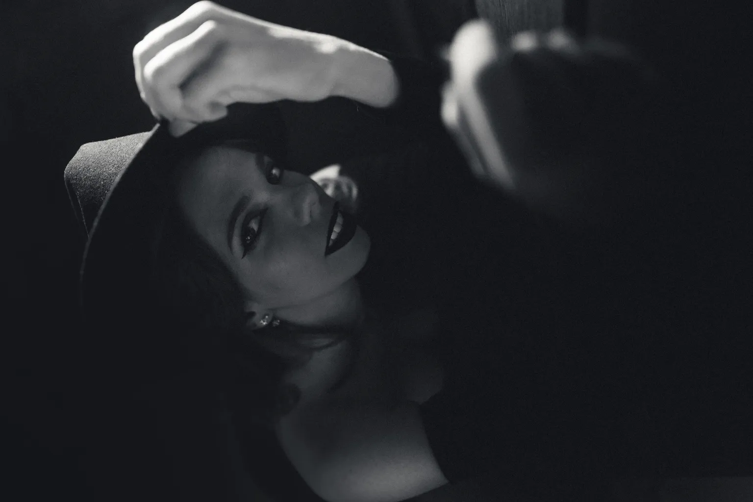 Moody black-and-white editorial close-up of a smiling woman lying back, a hand resting at the edge of frame.