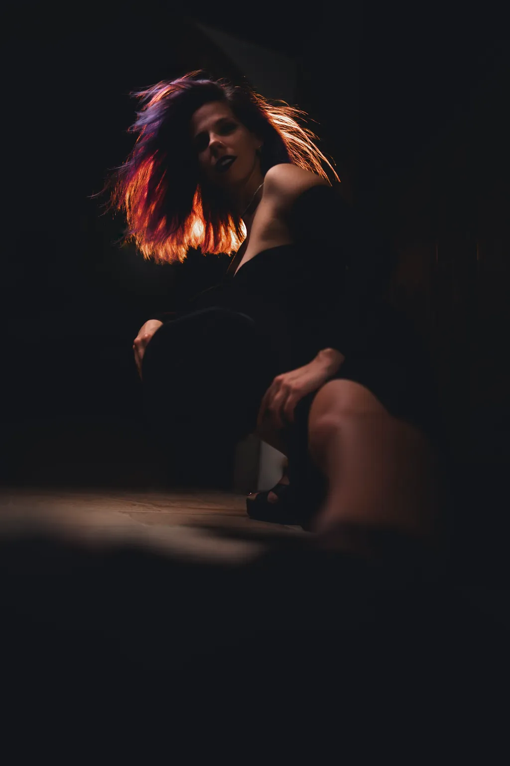 Editorial portrait with motion: a woman's hair swept in colored light, her seated form fading into darkness.