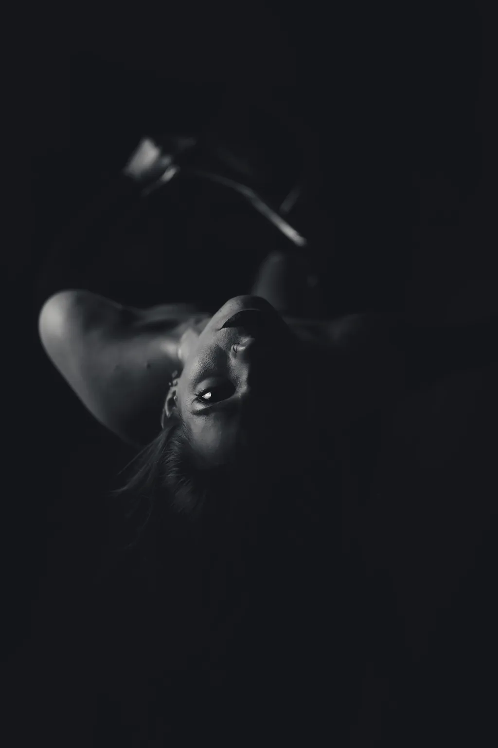 Minimal black-and-white noir portrait, Luxembourg: a woman's upturned face emerging softly from heavy shadow.