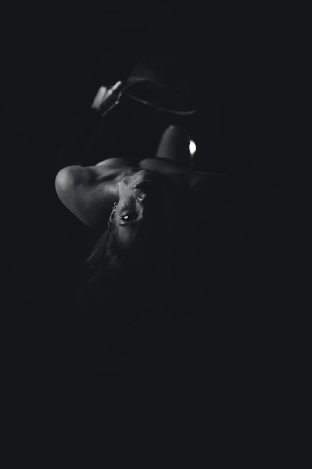 Subtle monochrome editorial portrait: a woman's profile barely lit, the frame dominated by deep black negative space.