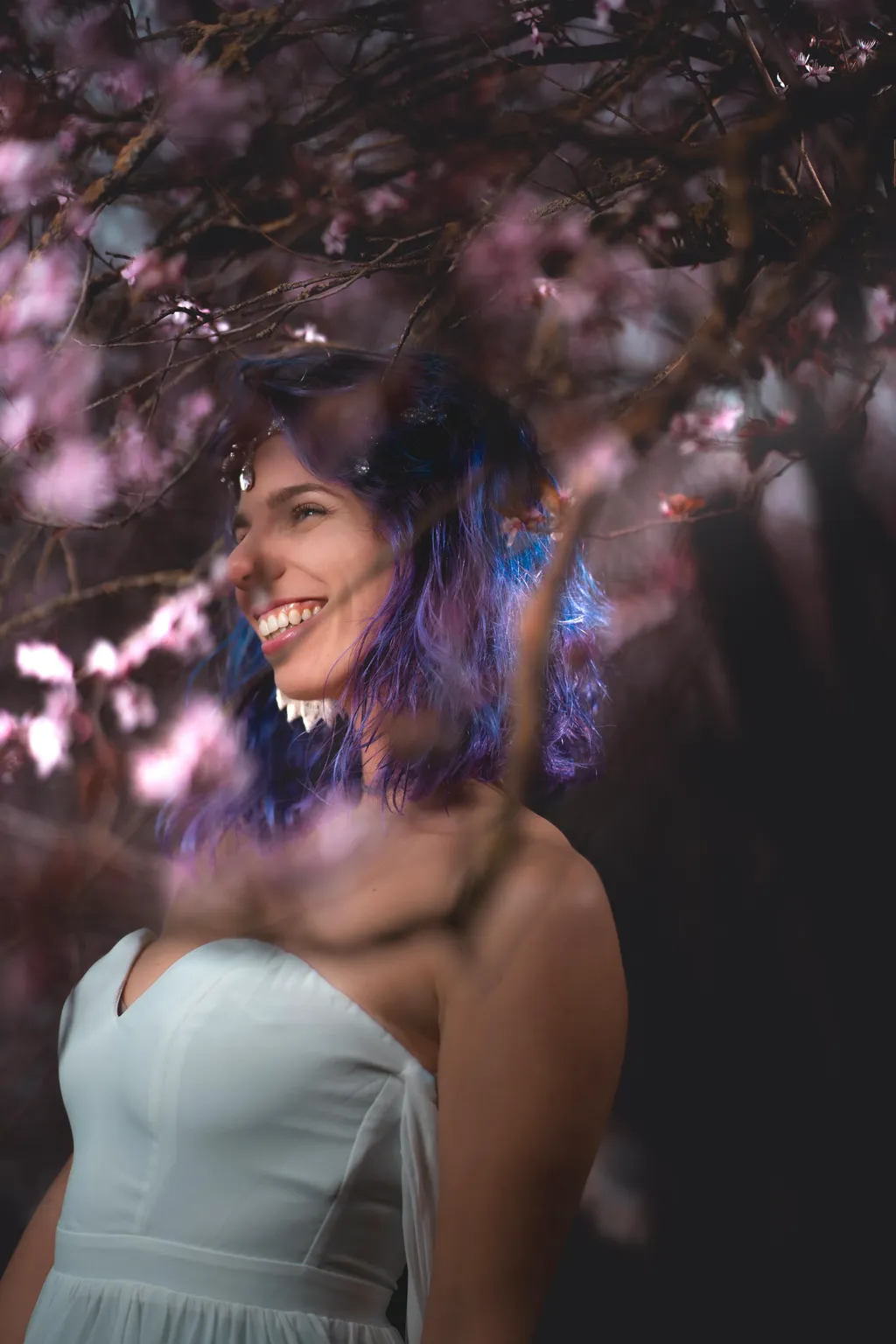 Joyful spring portrait of a smiling woman in a pale tulle gown, laughing beneath blooming cherry-blossom branches