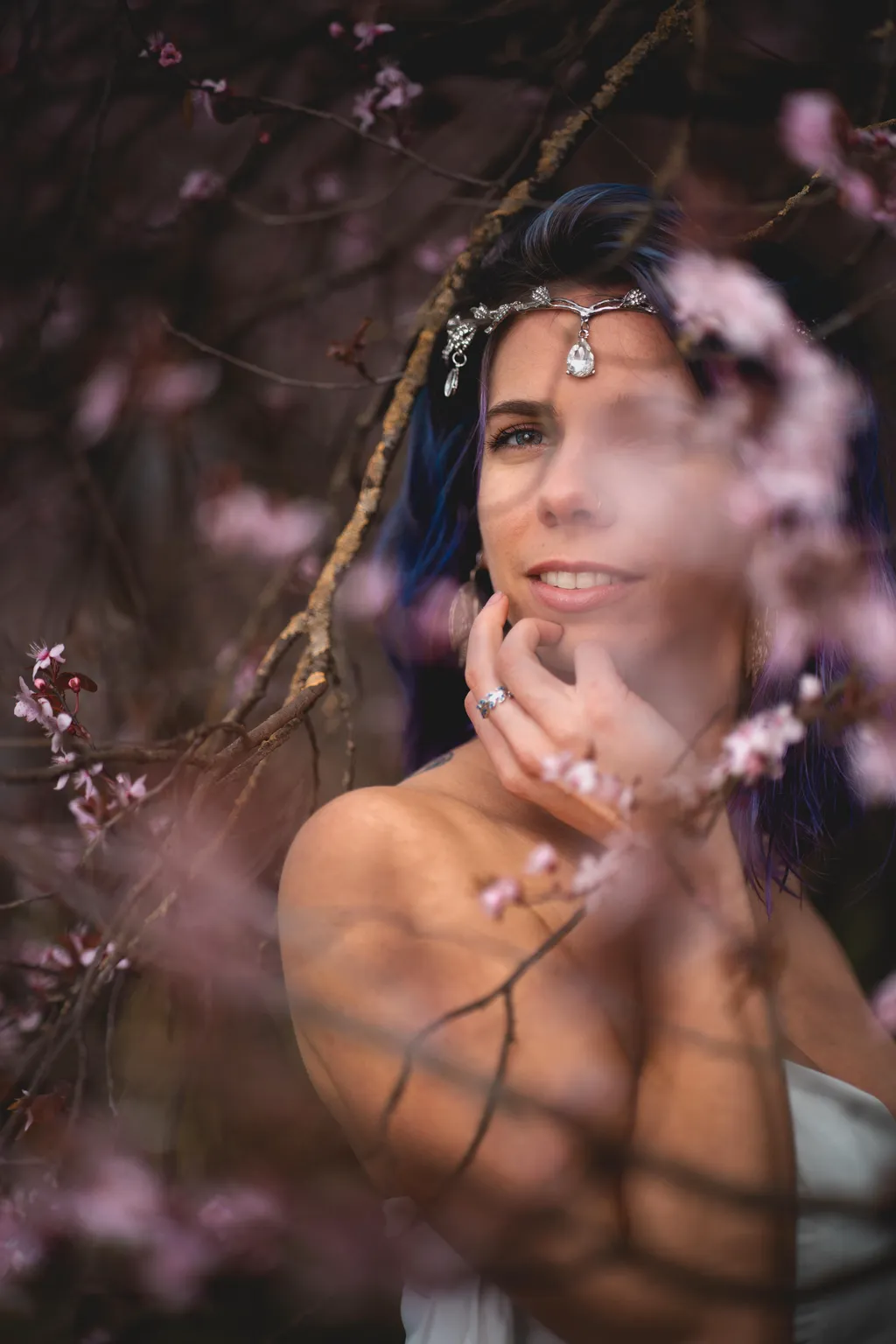 Dreamy Luxembourg portrait of a woman touching her face, dappled spring light through pink blossom branches