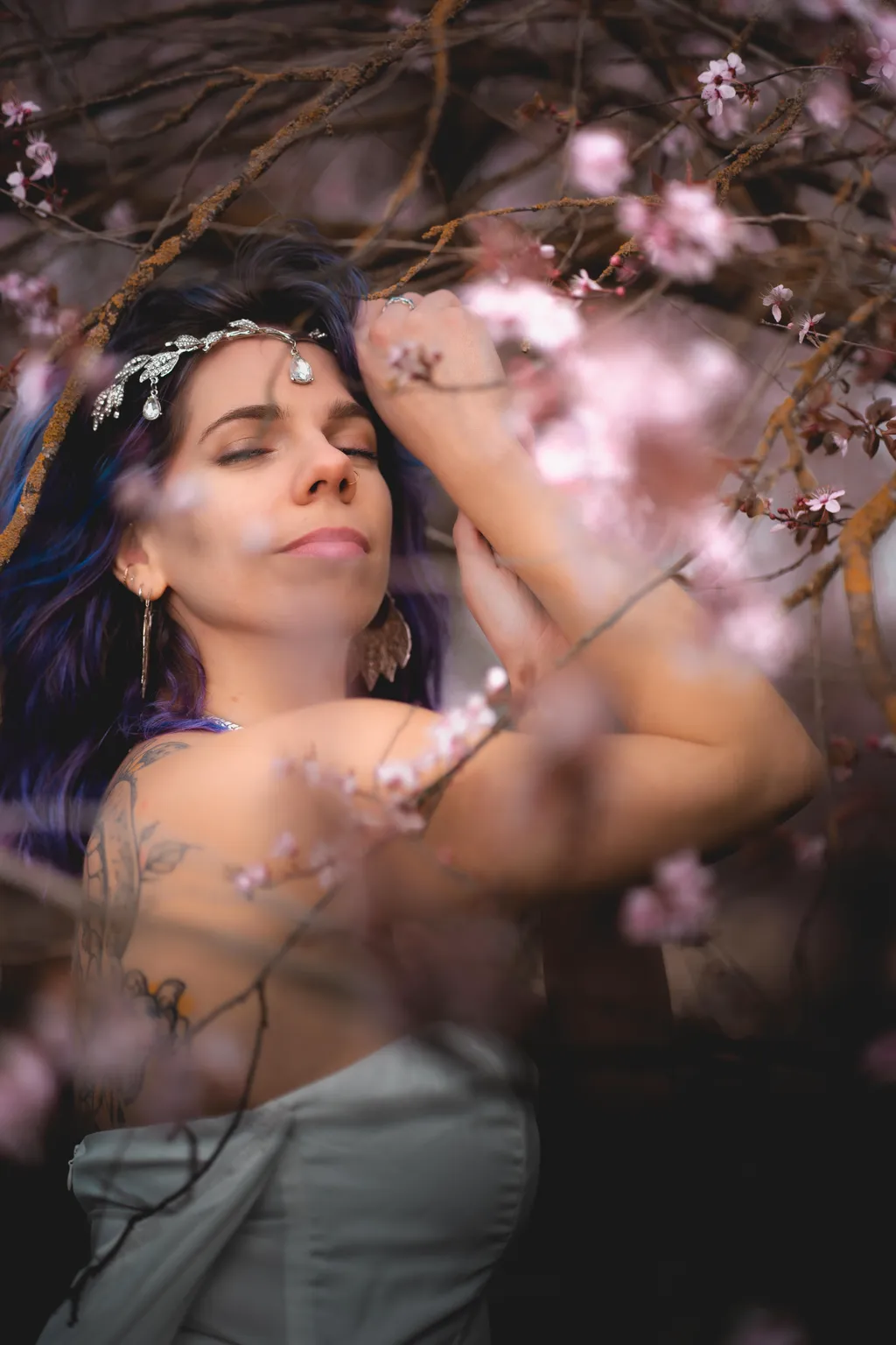 Soft, light-filled portrait of a woman with crossed arms, eyes closed, surrounded by spring blossom branches