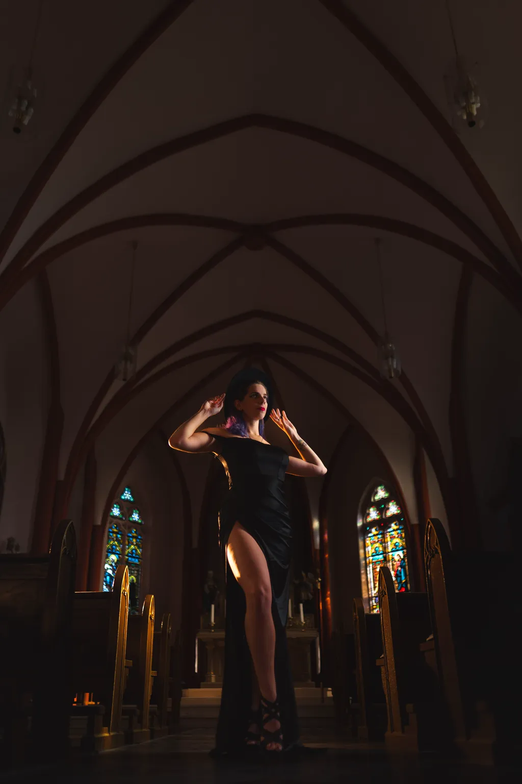 Editorial portrait of a woman in a black thigh-slit gown posing beneath the Gothic vaulted ceiling of a Luxembourg church