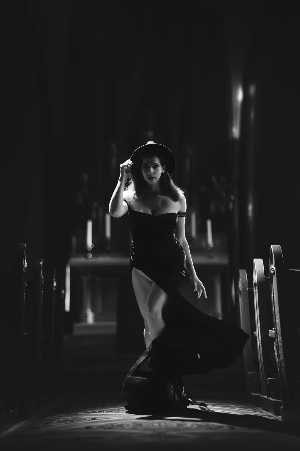 Black-and-white editorial portrait of a woman tipping her hat as she walks between pews in a darkened Luxembourg church