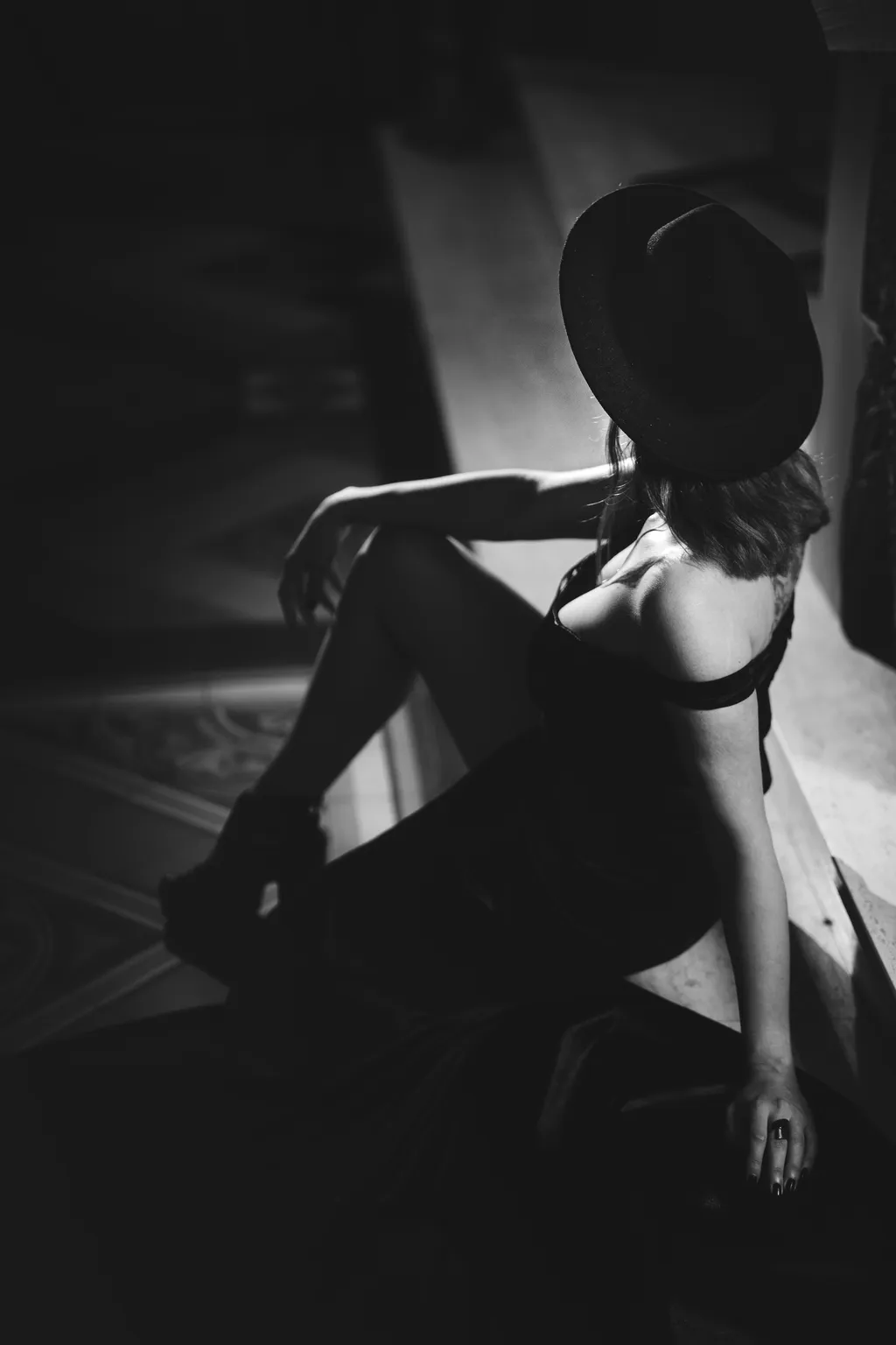 Moody black-and-white portrait of a woman in a hat seated low on a church floor, Luxembourg fine-art photography