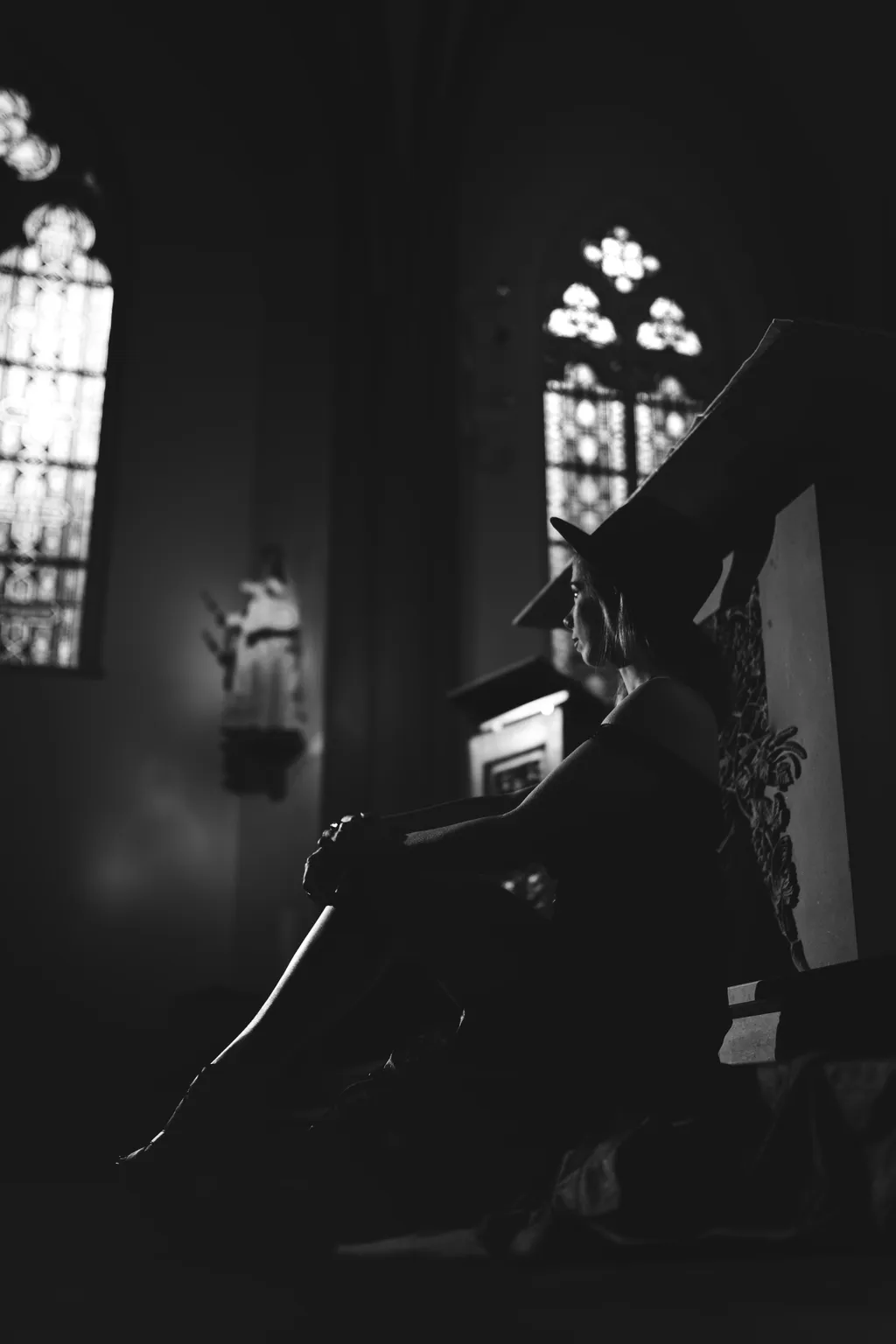 Silhouetted side profile of a seated woman in a hat against glowing stained-glass windows in a Luxembourg church