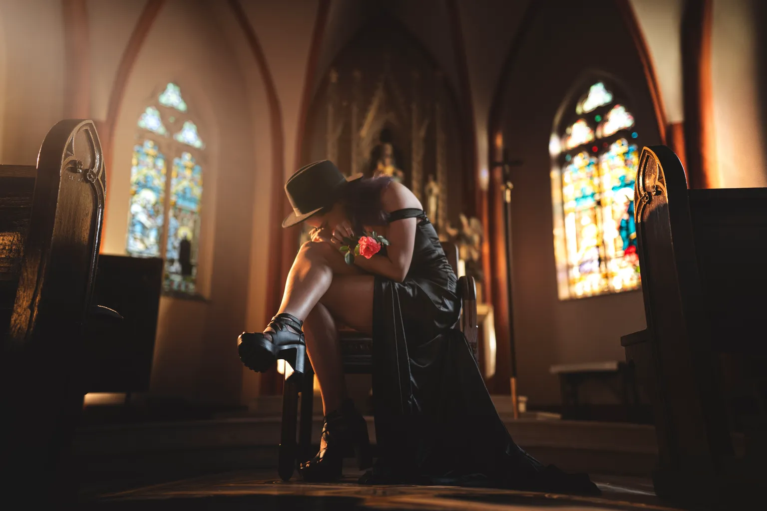 Editorial portrait of a woman in a black gown holding a red rose, seated in a sunlit Gothic Luxembourg church