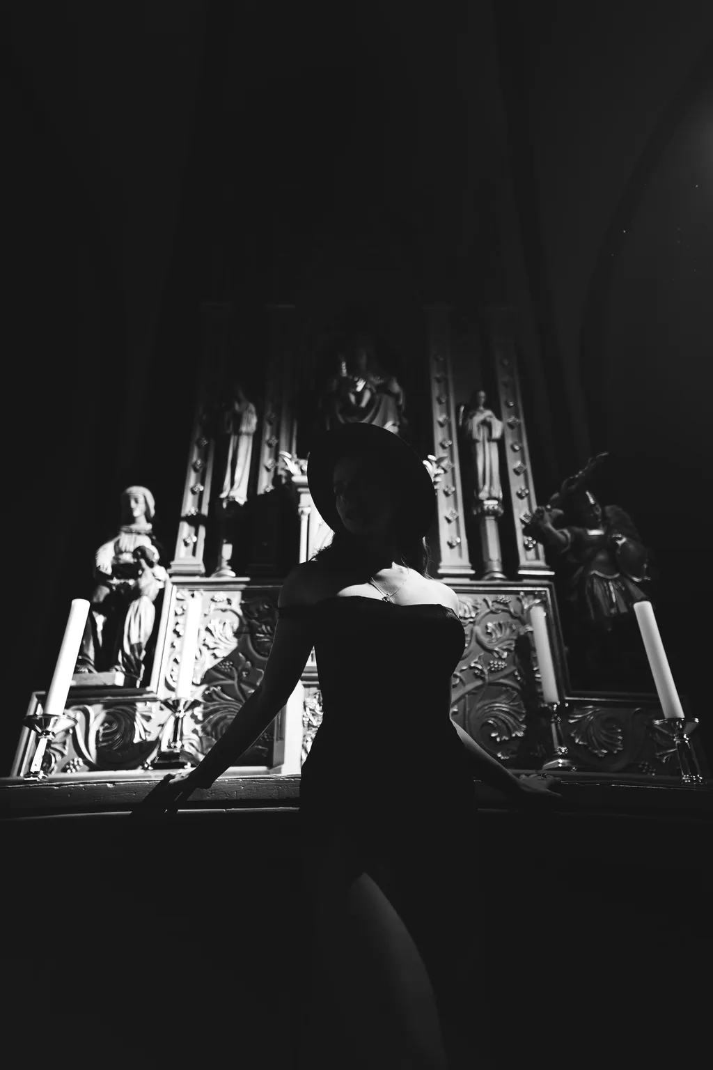 Black-and-white portrait of a woman in a hat standing before an ornate carved altar with statues, Luxembourg church